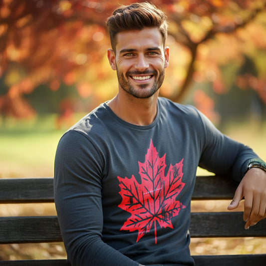 A man wearing a HGS Autumn's Wanderlust long-sleeve tee with a red maple leaf design, sitting on a bench in an autumn park.