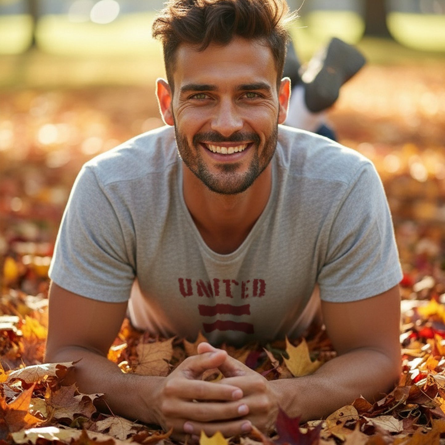 A man sitting in a pile of autumn leaves wearing a HGS United For Equality Heather Gray T-Shirt.