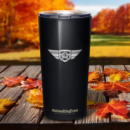 Black tumbler with a logo and text on a wooden surface with autumn leaves and trees in the background.