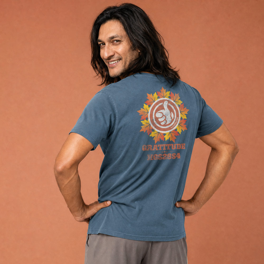 His Good Stuff's Autumn Catalog HGS26S4 Autumn Tee, back, relaxed fit, 100% ring-spun cotton, blue, short-sleeve, on a model against a flat Brandied Melon background. Graphic displays a large distressed HGS Fall thumbs-up icon with the letters "GRATITUDE" and "HGS26S4 underneath.