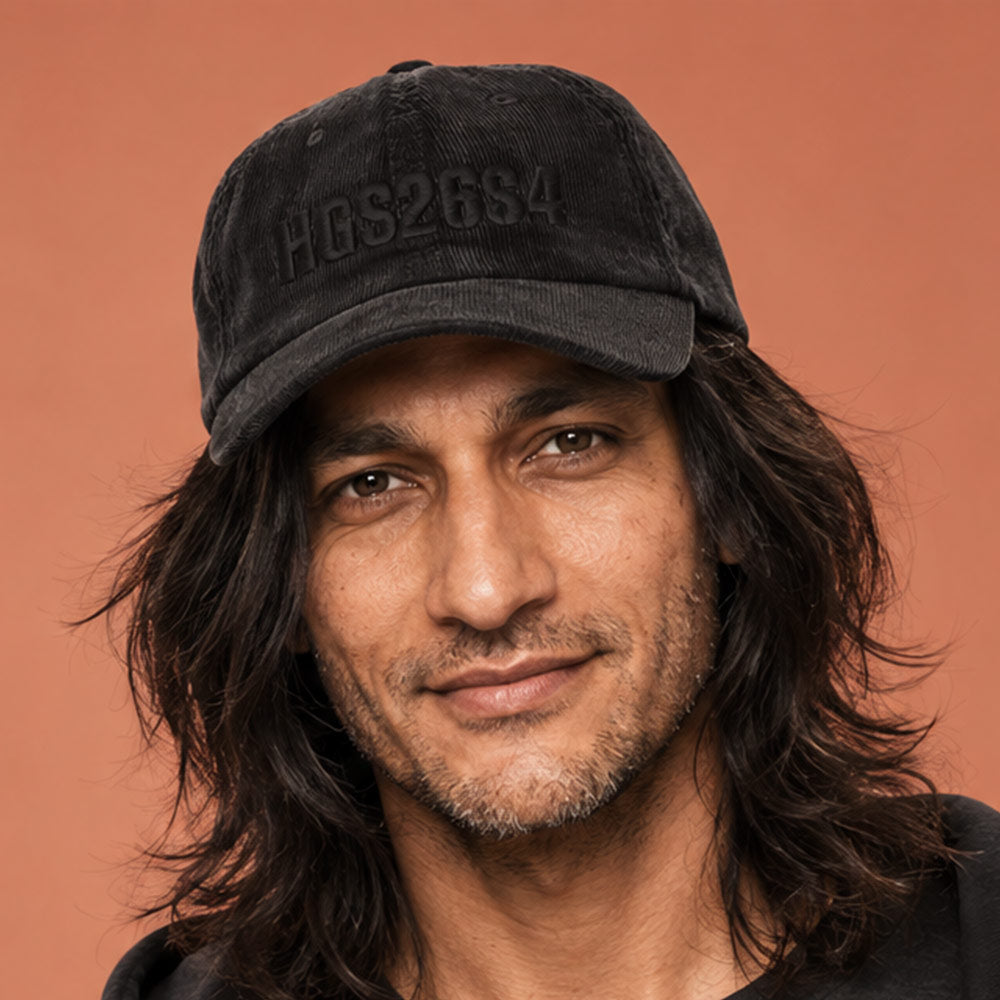 His Good Stuff's Autumn Catalog HGS26S4 Corduroy Cap, front closeup, 100% cotton corduroy with an adjustable golden buckle in the back, on a model against a flat Brandied Melon background. Graphic displays in black thread, 3-D embroidered HGS26S4
