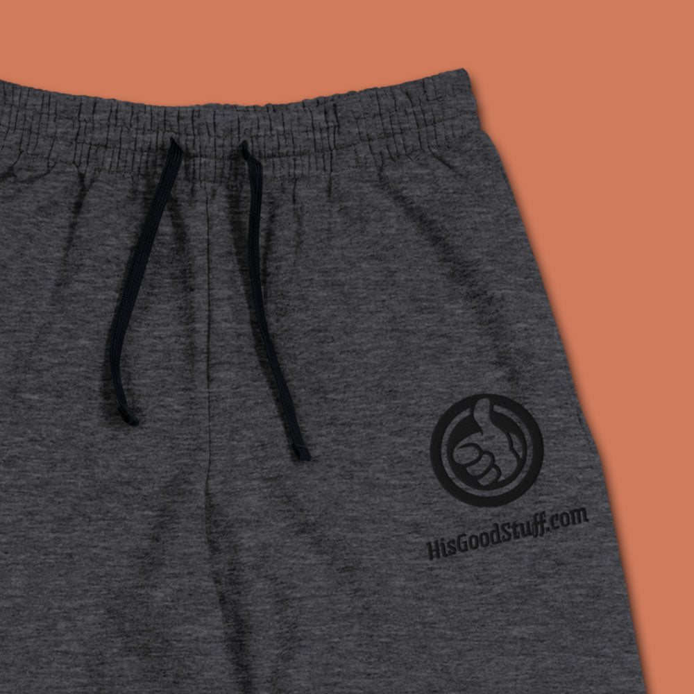 His Good Stuff's Autumn Catalog HGS26S4 Fleece Joggers, front fabric detail, tapered fit, preshrunk fleece, heather black, on a model against a flat Brandied Melon background. Graphic displays in the top right a black thread embroidery of a HGS Fall thumbs-up icon over HisGoodStuff.com