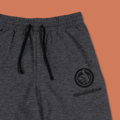 His Good Stuff's Autumn Catalog HGS26S4 Fleece Joggers, front fabric detail, tapered fit, preshrunk fleece, heather black, on a model against a flat Brandied Melon background. Graphic displays in the top right a black thread embroidery of a HGS Fall thumbs-up icon over HisGoodStuff.com