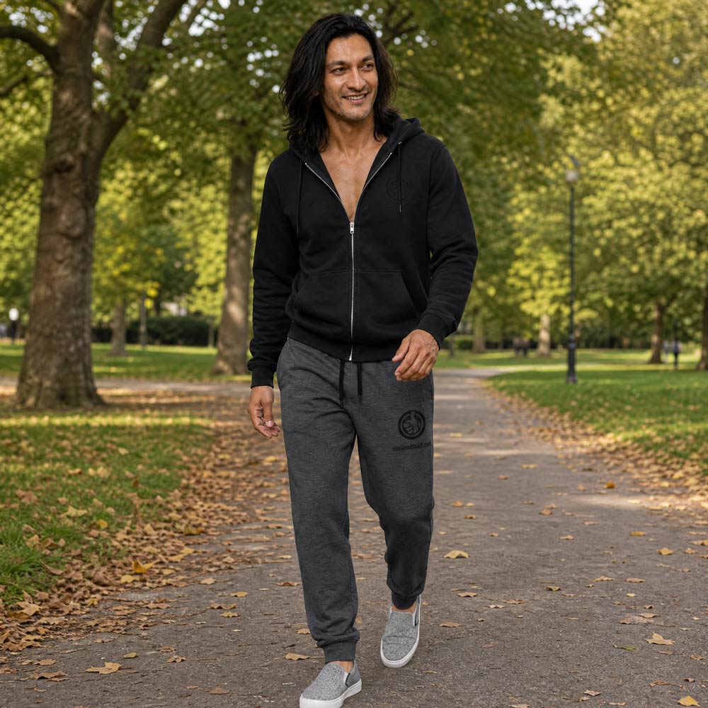 His Good Stuff's Autumn Catalog HGS26S4 Fleece Joggers, front, tapered fit, preshrunk fleece, heather black, on a model walking outside in a city park in Fall. Graphic displays in the top right a black thread embroidery of a HGS Fall thumbs-up icon over HisGoodStuff.com