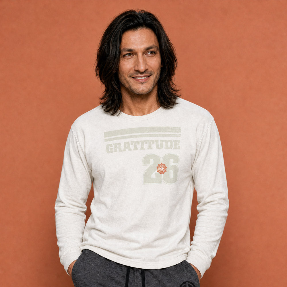 His Good Stuff's Autumn Catalog HGS26S4 Gratitude Jersey, front, heavyweight, 100% ring-spun cotton, white, long-sleeve, on model against a flat Brandied Melon background. Graphic displays two bars over distressed letters GRATITUDE, a number 26, and the HGS fall thumbs-up icon.