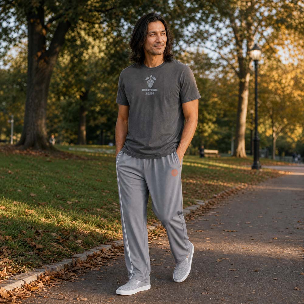 His Good Stuff's Autumn Catalog HGS26S4 Gratitude Tee, front, relaxed fit, 100% ring-spun cotton, grey, short-sleeve, front, on a model walking outside in a city park in Fall. Graphic displays an acorn graphic above the letters "GRATITUDE" and "HGS26S4".