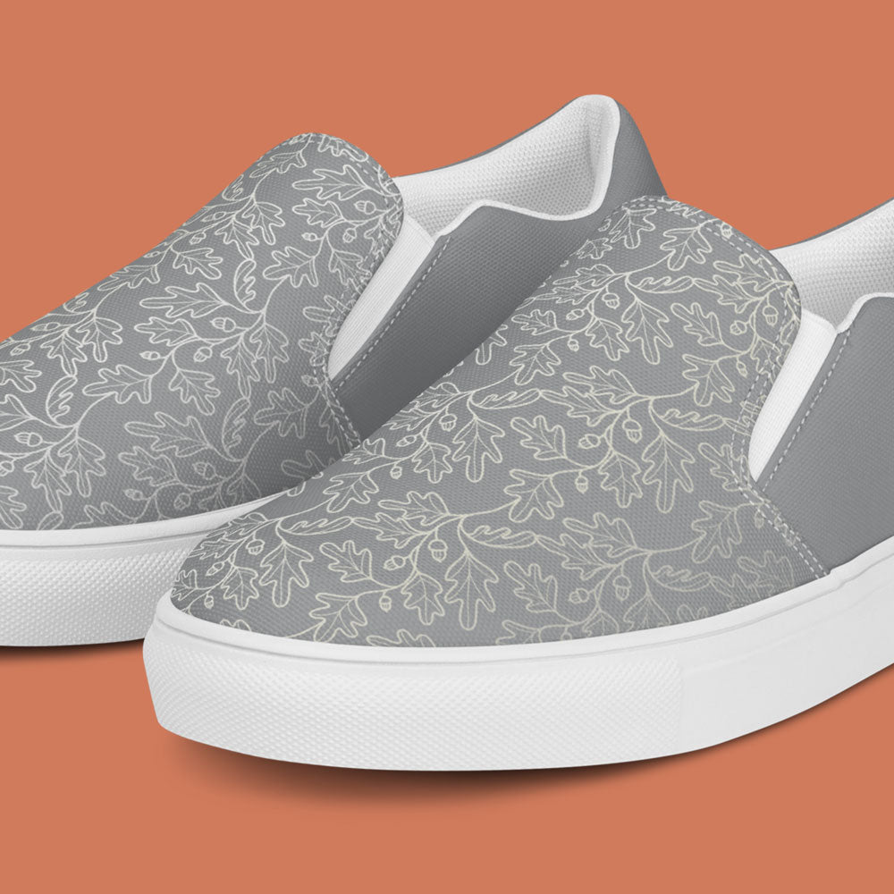 His Good Stuff's Autumn Catalog HGS26S4 Slipper Shoes, detail view, breathable lining, soft insole, elastic side accents, padded collar and tongue, on a flat Brandied Melon background. Ultimate Gray with cloud dancer white oak leaf floral pattern over the toes. 