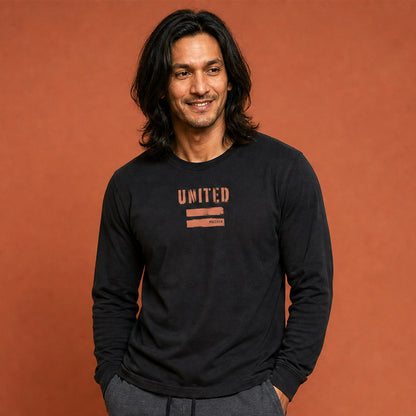 His Good Stuff's Autumn Catalog HGS26S4 United Equality, front, close up, heavyweight, 100% ring-spun cotton, black, long-sleeve, detail of fabric against a flat Brandied Melon background. Graphic displays two bars beneath the distressed letters "EQUALITY".