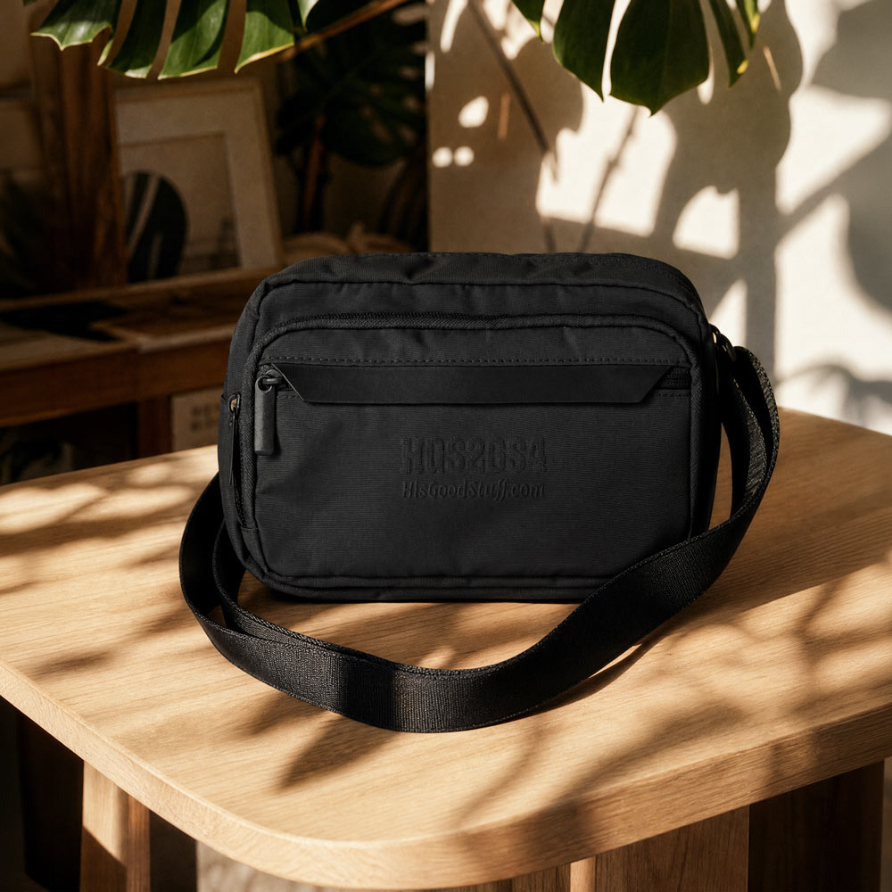His Good Stuff's Autumn Catalog HGS26S4 Urban Bag, front view, sleek, functional design with an adjustable shoulder strap and a secure zip closure, in and everyday environment. Black with black-thread-embroidered letters "HGS26S4" and HisGoodStuff.com underneath