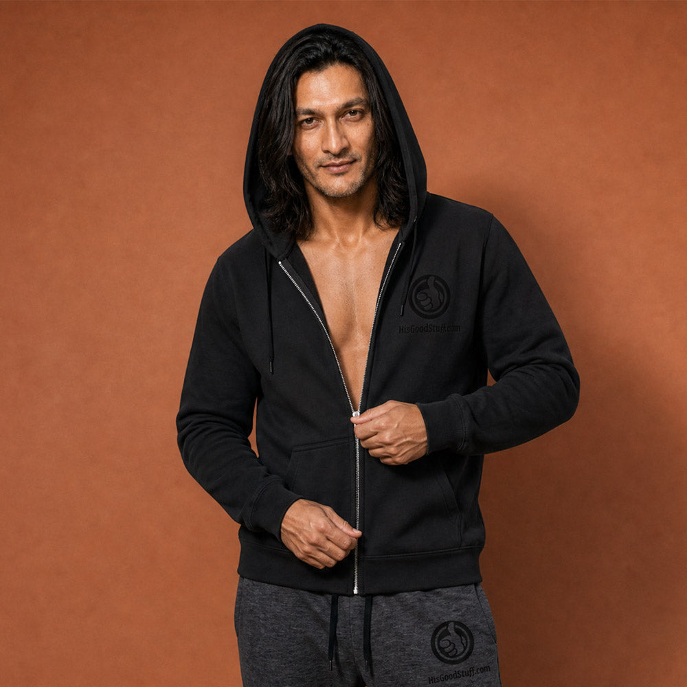 His Good Stuff's Autumn Catalog HGS26S4 Zip Hoodie, front closeup, relaxed fit, black fleece, matching round drawcord with metal eyelets and tipped end, on a model against a flat Brandied Melon background. Graphic displays in the top right a black embroidered HGS Fall thumbs-up icon with HisGoodStuff.com underneath