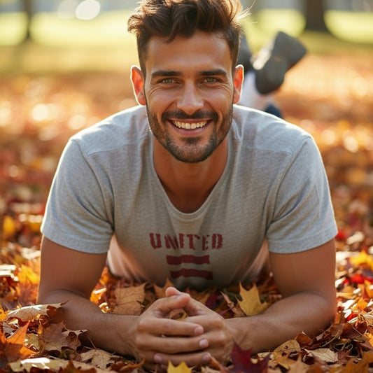 A man sitting in a pile of autumn leaves wearing a HGS United For Equality Heather Gray T-Shirt.
