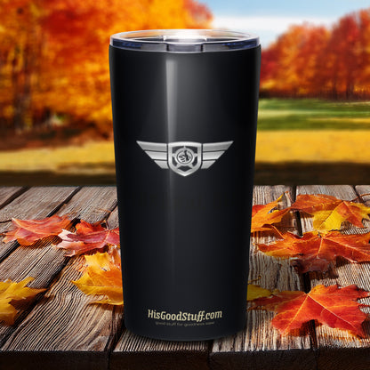 Black tumbler with a logo and text on a wooden surface with autumn leaves and trees in the background.
